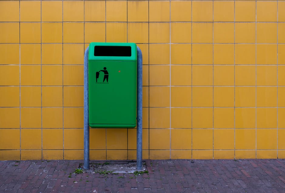 This image shows a large outdoor collection of waste and recyclable materials, primarily consisting of numerous stacked cardboard fruit delivery boxes with colorful labels, placed on a paved surface. 